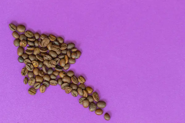 Kahve çekirdekleri mor arka planda bir ok şeklinde serilmiştir. Kahvenin artan fiyatı, büyüyen tüketim