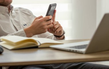 Yaklaş, iş adamı ahşap masada cep telefonu kullanıyor. Ofiste çalışırken akıllı telefon kullanan adam masadaki dijital tablet, sosyal ağ, iş başarısı