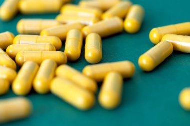 Koyu yeşil arka planda bir avuç sarı tıbbi kapsül.,