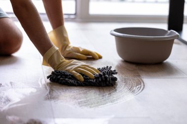 Sarı koruyucu eldivenli bir adam elleriyle yerleri yıkıyor.