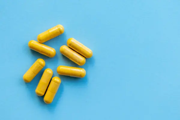 Bir avuç sarı tıbbi kapsül, parlak mavi arka planda haplar.