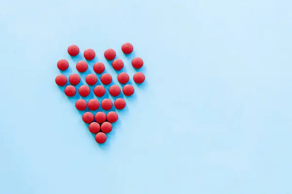Sağlıklı kalp, kalp hastalığı ve benzeri konularda soyut. Parlak mavi arka planda kalp şeklinde parlak kırmızı haplar.