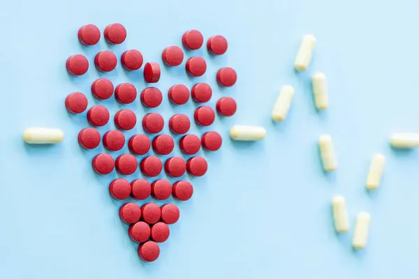 Sağlıklı kalp, kalp hastalığı ve benzeri konularda soyut. Parlak mavi arka planda kalp şeklinde parlak kırmızı haplar.