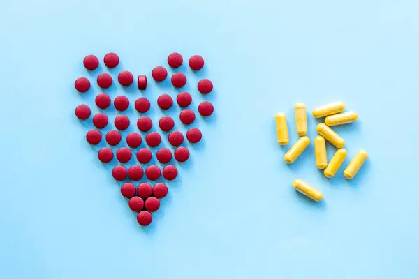 Sağlıklı kalp, kalp hastalığı ve benzeri konularda soyut. Parlak mavi arka planda kalp şeklinde parlak kırmızı haplar.