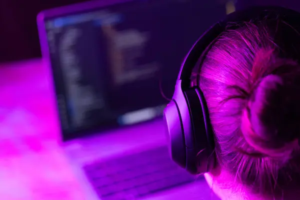 Yazılım geliştirme ve bilişim eğitimi konuları için uygun, neon mor ışıkta ekranda yazılım kodu olan dizüstü bilgisayarın önündeki kişi 