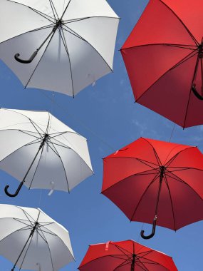 Mavi arka planda asılı kırmızı ve beyaz şemsiyeler 