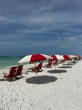 Zümrüt Sahili 'nde kırmızı ve beyaz plaj şemsiyeleri ve sandalyeler. 