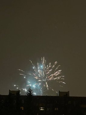 Gece gökyüzünde bir apartmanın arkasında havai fişekler patlıyor.