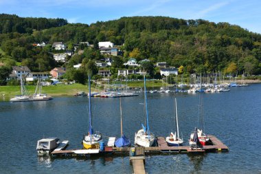 Eifel 'deki Rursee Gölü, küçük yelkenli tekneleri limanıyla Woffelsbach köyünü ziyaret ettiğinizde özel çekiciliğini gösterir..