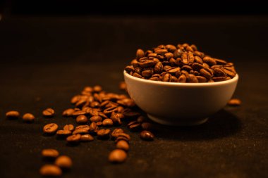 Beyaz bir fincanın yanında taze kavrulmuş kahve çekirdekleri.