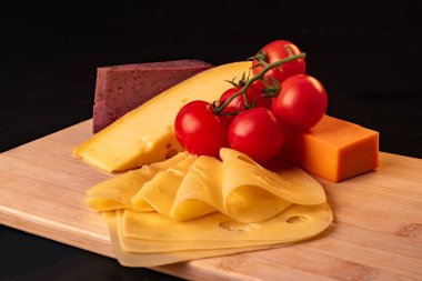 Tahtada duran sarı peynir, turuncu peynir, lavanta peyniri ve domates kompozisyonu, yakın plan..