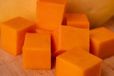 Turuncu peynir küpleri ve ahşap bir tahtanın üzerinde büyük bir parça sarı peynir..