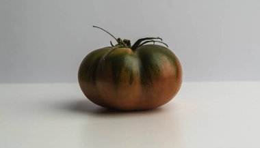 Yeşil tonlu olgun kırmızı domates, basit beyaz bir arka planda eşsiz biçimini ve dokusunu gösteriyor.