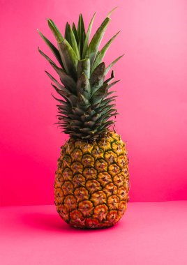 Canlı pembe bir arkaplanda basit ama çarpıcı bir kompozisyonda sergilenen taze ananas.