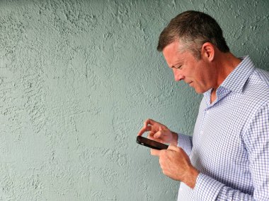 X kuşağı genç adam mavi arka planda cep telefonuyla mesajlaşıyor.. 