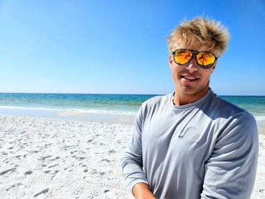 Sahilde yansıtıcı güneş gözlükleriyle poz veren havalı sörfçü çocuk..