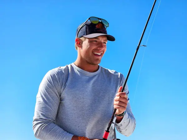 Genç adam Millennial yazın mavi gökyüzüne karşı sahilde balık tutuyor.. 