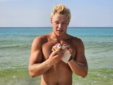 Genç üstsüz adam Millennial yaz tatilinde Florida sahilinde kahvaltıda çörek yiyor.. 