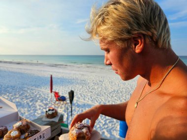 Yakın plan, işten önce Florida sahilinde kahvaltıda çörek yiyen yakışıklı bin yıllık bir adam..