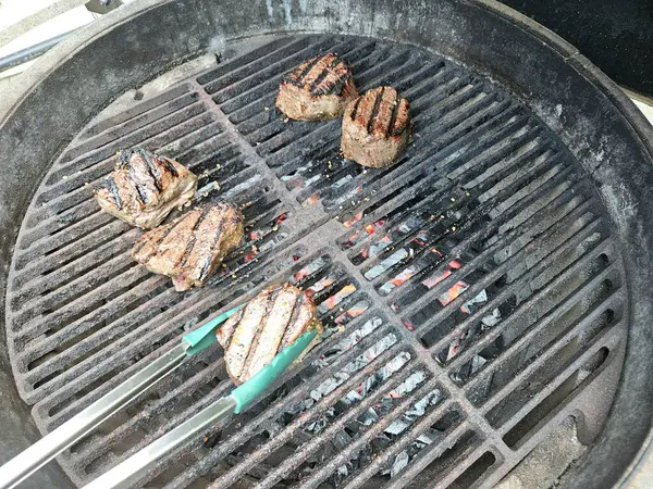 Ev sahibi akşam yemeği için mangal ızgarası fileminyonu pişiriyor..