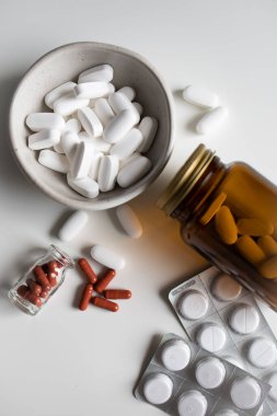 Beyaz arka planda şişelerden farklı haplar ve kapsüller döküldü.