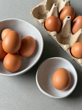 Kağıt tepside kahverengi tavuk yumurtası ve gri arka planda mutfak kaseleri.