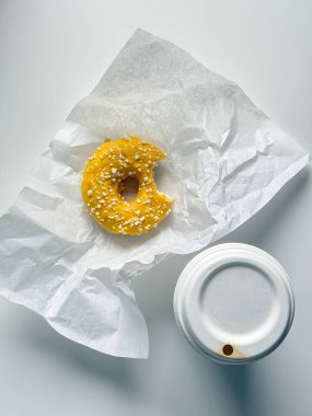 Beyaz kağıtlı sarı çörek beyaz ofis masasında ve kahve fincanı paket.