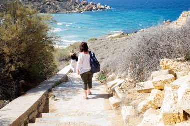 Sırt çantalı bir kadın turist Malta 'daki Riviera halk plajında denize iniyor.