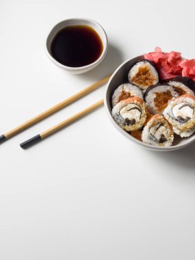 Suşi, pembe zencefil, soya sosu ve beyaz masa manzaralı tahta çubuklarla dolu bir kasede yuvarlanıyor.