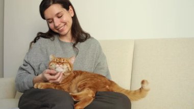 Kız nazikçe kızıl kedilerinin boynunu tırmalıyor ve onu sevgiyle okşuyor.