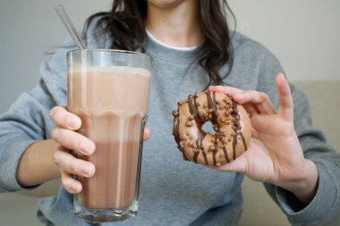 Büyük bardakta kakao ve kızın ellerinde kahverengi kapuçino çöreği.