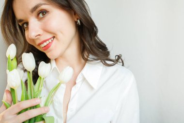 Gülümseyen, esmer, beyaz laleli genç bir kadın. Fotokopi alanına yakın.