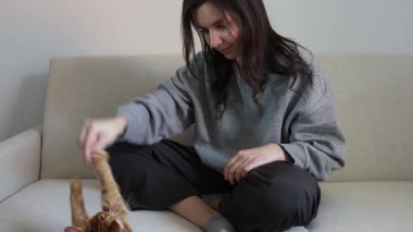 Evdeki kanepede oturan ve kedisine lezzetli şeyler ikram eden bir kız.