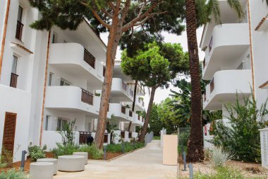 Cala d 'Or köyünde yeşil tropikal ağaçlar ve kozalaklı bitkilerle dolu beyaz minimalist otel bölgesi. İspanya 'daki Mallorca Adası