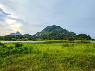 Yeşil çimenli güzel bir dağ manzarası ve Tasik Timah Tasoh, Perlis, Malezya 'da bulutlu mavi bir göl..