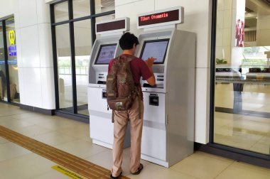 A man is at KCIC Halim Station using a ticket vending machine. The man in the backpack taps the touchscreen to buy and print a train ticket, Jakarta, Indonesia, May 30, 2024. KCIC Halim Station, High Speed Rail. clipart