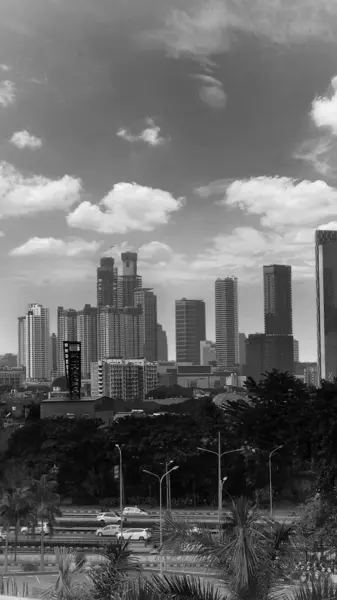 stock image Cityscape of Jakarta City with tall buildings under the clouds. Indonesia, on May 30 2024.Trees provide shade for cars passing al ong the highway.