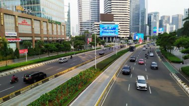 Güzel şehir manzarası ana yoldaki yüksek binalarla çevrili ve LCD panolarından reklamlar var. Jakarta. Endonezya, 4 Ağustos 2024. Araçlar öğleden sonra Sudirman karayolundan geçiyor.. 