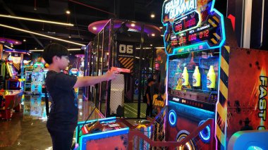 Genç tek başına oyun makinesine nişan alıyor. Genç bir çocuk alışveriş merkezinin eğlence alanında oyun makinesine ateş ediyor. Depok, Endonezya, 15 Şubat 2025. Yeni ve modern teknolojiyle eğlenceli oyun makinesi.