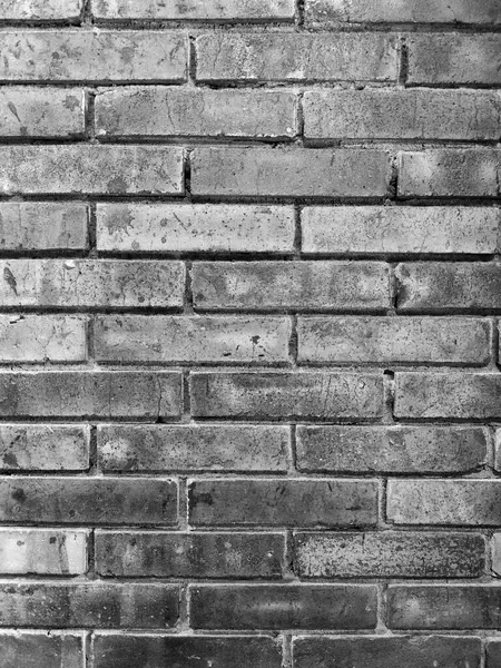 Üzerinde çatlaklar, lekeler ve pürüzlü yüzeyler olan pürüzlü bir tuğla duvar. Eski tuğlalar ve koyu harç hatları derinlik ve kontrastı ekler. Siyah ve beyaz duvar resmi tuğlalıyor.