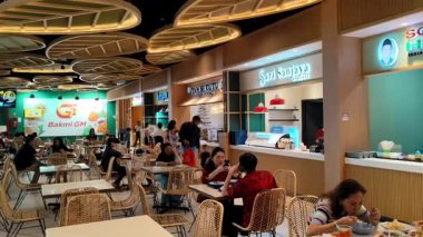 İnsanlar yemekhanede, aileleri ve arkadaşlarıyla sohbet ederken çeşitli yemek seçimlerinin tadını çıkarıyorlar. Jakarta, Endonezya, 15 Nisan 2025. Kelapa Gading Mall 'da çeşitli yemek stantları var..