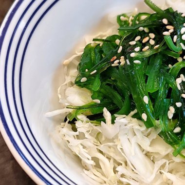 Deniz yosunlarının parlak yeşil rengi ve susam serpintisi tadını artırıyor. Taze yeşil susamlı deniz yosunu salatası. Taze beyaz lahananın üstünde.. 