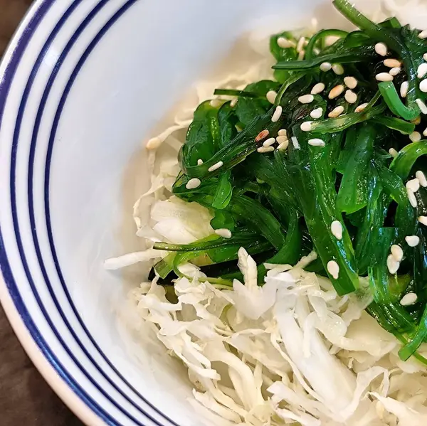 Deniz yosunlarının parlak yeşil rengi ve susam serpintisi tadını artırıyor. Taze yeşil susamlı deniz yosunu salatası. Taze beyaz lahananın üstünde.. 