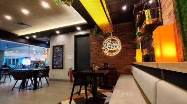 Gloria Jeans Cafe 'nin modern ve rahat iç mekanı, yolculara rahat bir atmosfer sağlayan, yumuşak, sarımsı ve kremsi tonlarıyla, ılık bir ortam yayıyor. Bali, Endonezya, 2 Temmuz 2025.