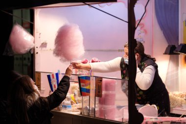 Leon, İspanya - 28 Aralık 2021: Kadın, panayır festivalinde ya da karnavalda uzanan küçük bir kıza pamuk şeker veriyor.
