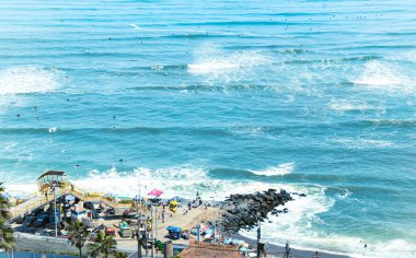 A vibrant scene captured at Miraflores's Costa Verde Beach, where surfers ride the waves while beachgoers stroll along the coast on a sunny day clipart