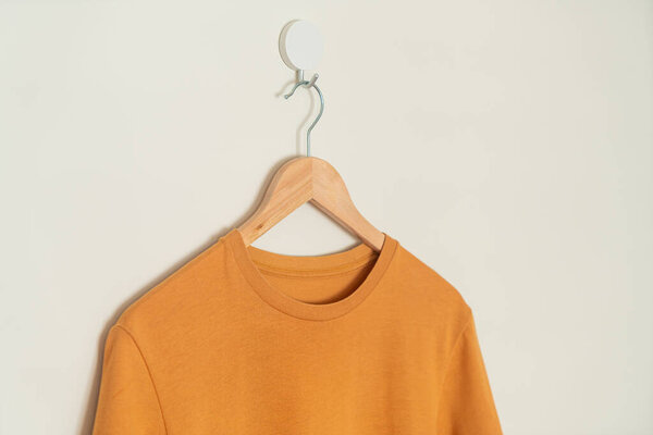 orange t-shirt hanging with wood hanger on wall