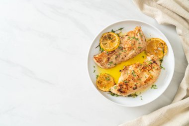 Beyaz tabakta tereyağlı ızgara tavuk, limon ve sarımsak.