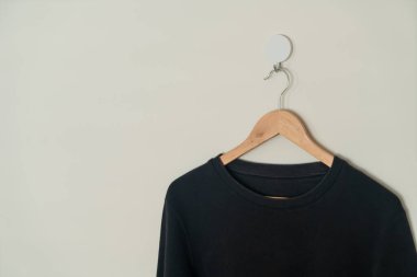black sweater hanging with wood hanger on wall
