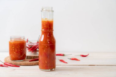 Şişede kırmızı biber ya da kırmızı biber sosu ve arka planda kavanoz.